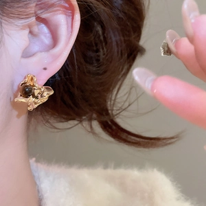 Macro view of gold lava-style earrings with dark stone inlay on a model's ear