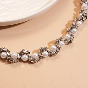 Detailed view of silver metal chain interwoven with round white pearls on beige surface