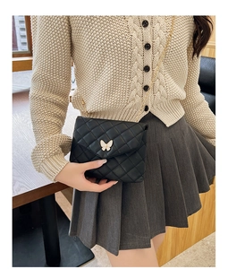 Detail of black quilted crossbody bag featuring a white butterfly clasp and gold chain strap