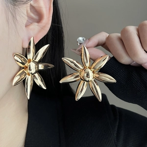 Close-up of a large gold floral stud earring worn by a model in a minimalist style