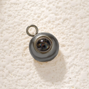 Macro view of a round stainless steel charm with a central rainbow reflective projection stone
