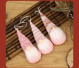 Three pink knit Christmas gnome ornaments with white hanging ribbons on rustic wood