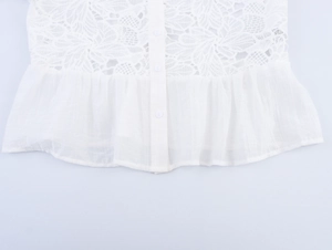 Detail of white blouse featuring delicate lace trim, ruffles, and buttons on the hemline