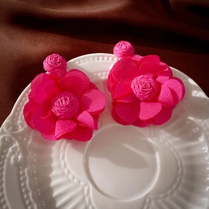 Détail macro de boucles d'oreilles fleurs en dentelle de raphia magenta sur plat