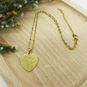 Detail of 18K gold heart pendant necklace with hammered texture on a wooden tray