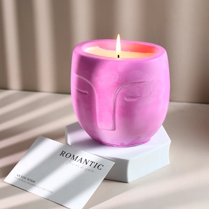 Light pink face-shaped ceramic candle jar with relief art and glowing white wax