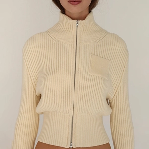 Detail of slim-fit beige ribbed knit sweater featuring a full zipper and front patch