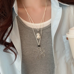 Detailed view of layered necklace featuring a floral pendant and baroque pearl on cords