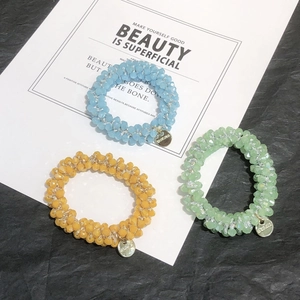 Detail of three elastic beaded hair ties in blue, yellow, and green with gold charms