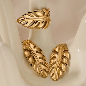 Golden monstera leaf jewelry set with earrings and ring on a white ceramic hand display