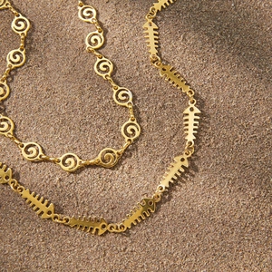 Detailed close-up of golden fishbone and spiral chain necklaces on a sandy beach