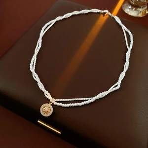 Detail of double-layer necklace with pearl chain and gold starburst compass pendant