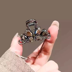 Detail of a small metal hair claw clip featuring grey crystal flowers held by a hand