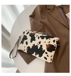 Detail view of cow print envelope clutch with wristlet strap and black tassel charm