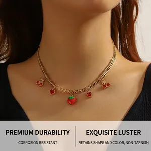 Detail of gold snake chain necklace with red strawberry and cherry charms on a model