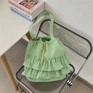 Detail of green plaid canvas tote bag featuring layered ruffle edges and drawstring closure
