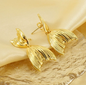Vue macro de boucles d'oreilles queue de poisson en or 18K sur un tissu en satin doré