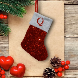 Close-up of mini red sequin Christmas stocking with letter Q embroidery on pine background