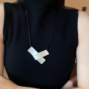 Close-up of modern geometric white pendant on black cord necklace worn on black clothing