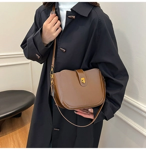 Close-up of a brown saddle bag with gold buckle worn by a model in a minimalist setting
