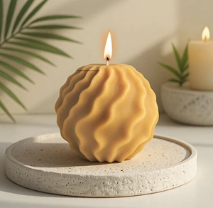 Close-up of a lit yellow spherical wave candle on a stone tray with soft lighting