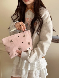 Pink corduroy makeup bag with cute bear embroidery and heart details held by a model