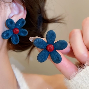 Macro detail of navy blue flocked flower earring with a red bead center on model