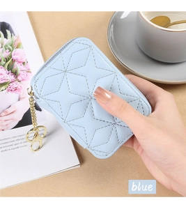 Blue quilted mini cosmetic bag with gold zipper and keychain held in hand over desk