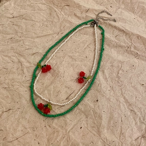Detail of double-layer necklace featuring green beads and red cherry pendants