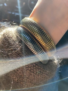 Dettaglio di grossi bracciali oro e argento a onde testurizzate sopra un maglione marrone