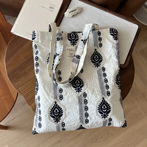 Beige cotton linen tote bag with black ethnic embroidery on a rustic wooden table
