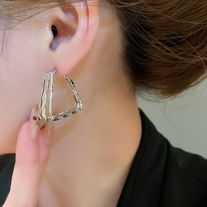 Close-up of layered silver geometric triangle earrings on a model with polished finish