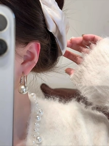 Detailed view of silver needle pearl earrings with cream white pearl on a model