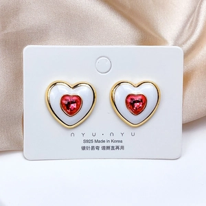 Detail of S925 silver heart earring with white enamel and centered red gemstone