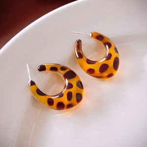 Macro shot of curved leopard print resin C-shaped hoop earrings on a ceramic dish