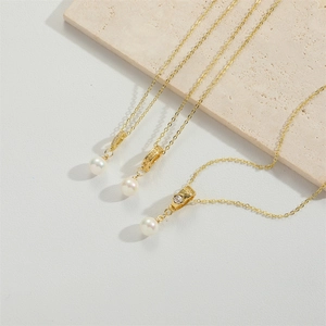 Three elegant gold-plated pearl pendant necklaces displayed on a beige natural stone base