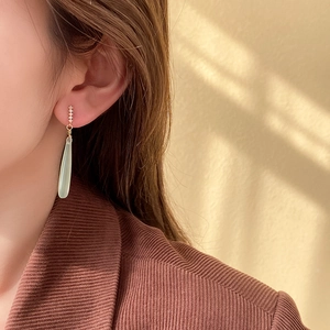Detail view of a green teardrop earring on model with elegant gold and zircon accents