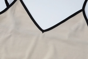 Détail du col en V côtelé beige avec finition contrastée noire sur le bord de la robe