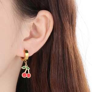 Close-up of red cherry pendants on gold stainless steel hoop earrings worn by a model