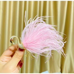 Detailed view of a golden flamingo brooch with zircons and pink feathers held by hand