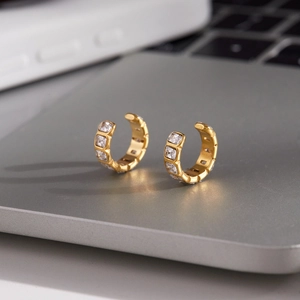 Gold-plated C-shaped ear cuffs with square zircons displayed on a metallic laptop surface