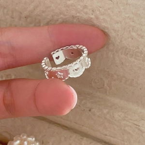 Gros plan détaillé de la bague argentée avec motifs cœurs et étoiles évidés et bords ondulés