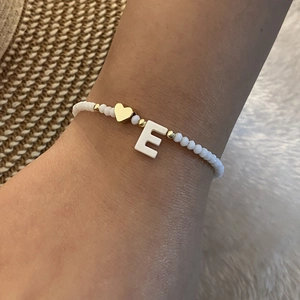 Detail of beaded bracelet with gold heart and letter E charm worn on a wrist