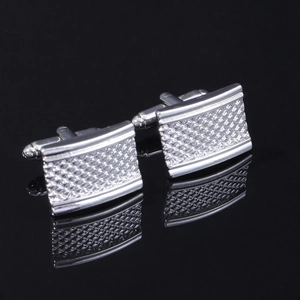 Close-up of silver square cufflinks with engraved stripes on a black reflective surface
