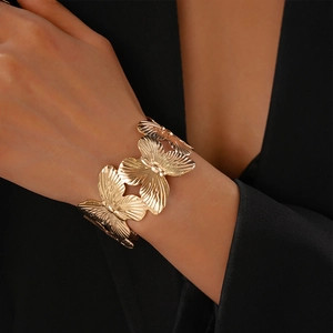 Close-up of golden metal butterfly open bangle with textured wings worn on a wrist