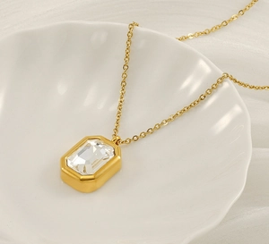 Detail of a square-cut zircon pendant on a gold chain displayed on a shell plate