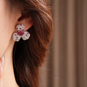 Close-up of vintage flower earrings with sparkling zircons and red gemstones on model