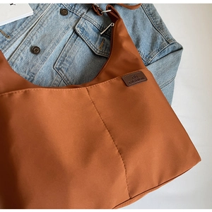 Detail of caramel nylon tote bag with leather logo tag on denim jacket background