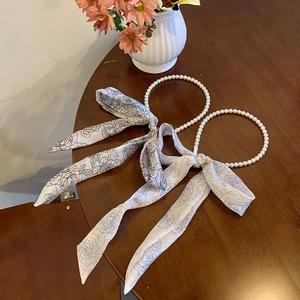 Detail of pearl headband and silk ribbon with blue floral print on a wooden background