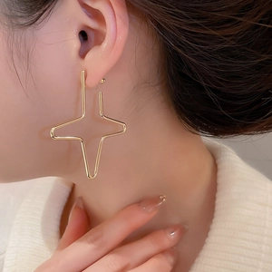 Close-up of golden geometric cross star earrings showing elegant minimalist style